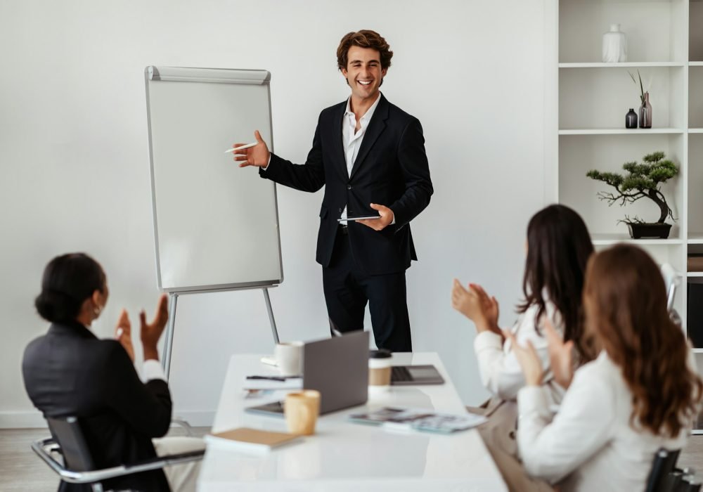 Happy male business trainer or team leader standing near whiteboard making presentation at meeting